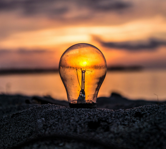 Lightbulb stuck in sand with sun viewed through the glass