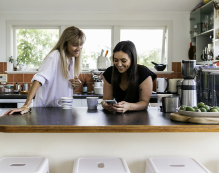 Women standing at kitchen bench looking at a phone