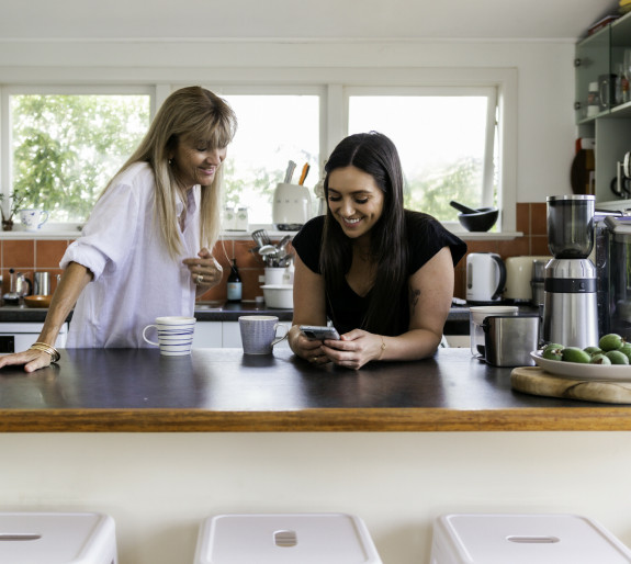 Women standing at kitchen bench looking at a phone